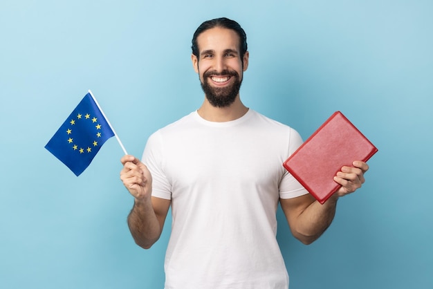 Uomo sorridente che tiene libro e bandiera dell'europa istruzione all'estero guardando la fotocamera con un sorriso a trentadue denti