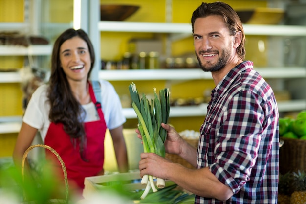 Uomo sorridente che tiene un mazzo di cipolline nel negozio di alimentari