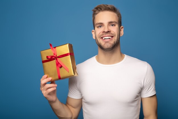 Smiling man holding golden gift isolated on blue