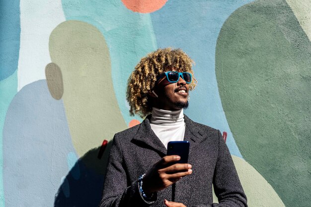 Foto uomo sorridente che tiene il telefono cellulare contro il muro