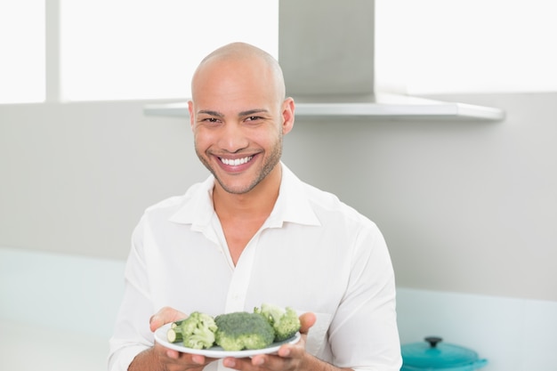 Smiling man holding a plate of broccoli in kitchen