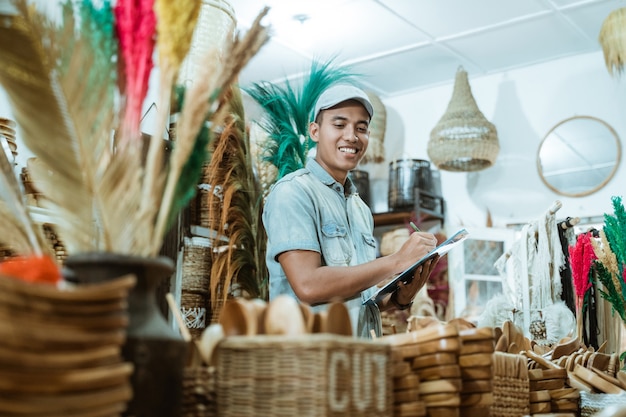 Smiling man holds the clipboard while list items among craft items in the craft gallery