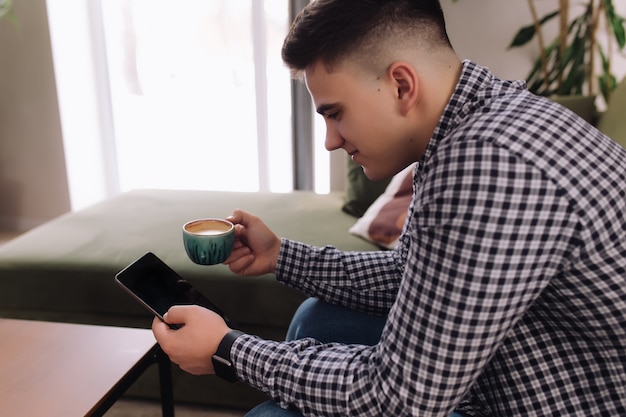 Uomo sorridente tiene e lettura smartphone con schermo nero e tazza di caffè