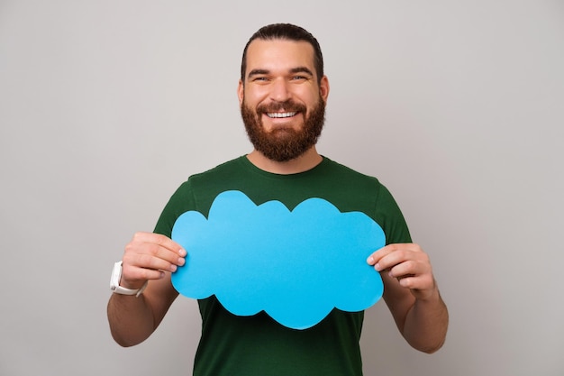 Smiling man is holds a blue cloud shaped bubble speech in front of him