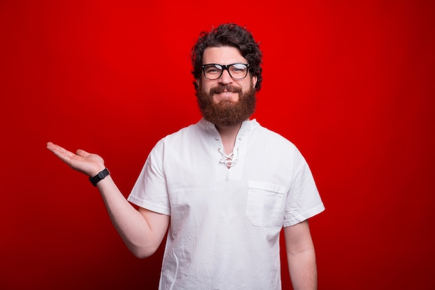 Smiling man is presenting something with his hand on red.