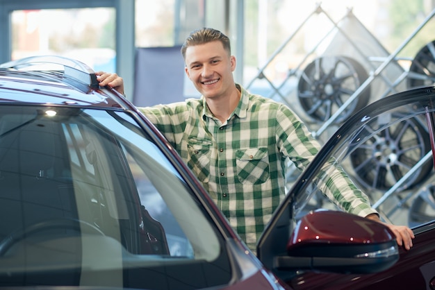 Smiling man leaning on car in dealership.