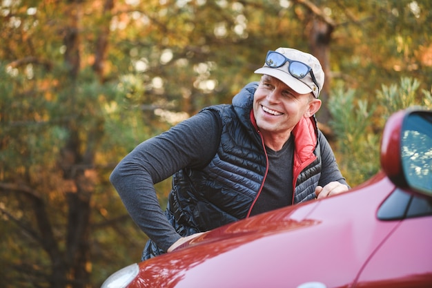 Smiling man leans on the hood of a red car