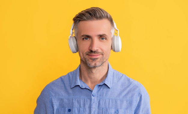 smiling man listen music in headphones on yellow background, technology.