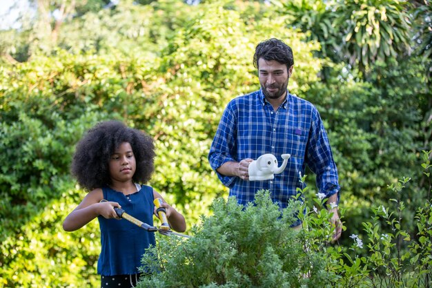 Smiling man looking at daughter cutting plants with hedge clipper