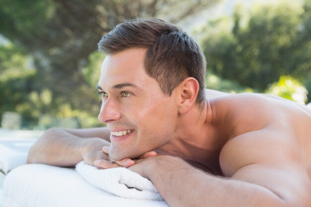 Smiling man lying on massage table poolside