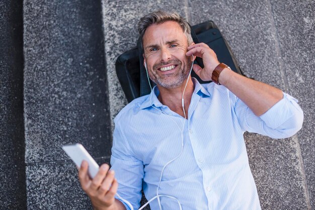 Smiling man lying on stairs with cell phone and earbuds