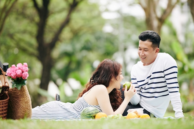 Улыбающийся человек предлагает подруге кусочек зеленого яблока на пикнике
