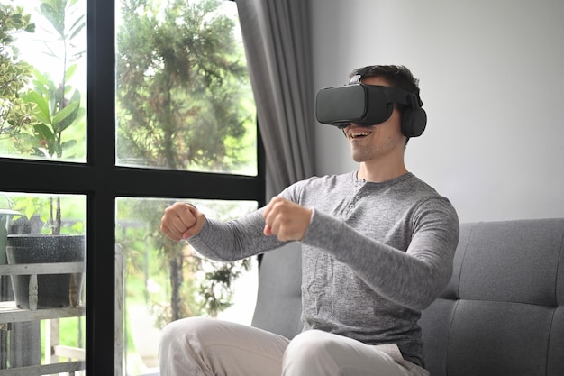 Smiling man playing video games with virtual reality headset at home