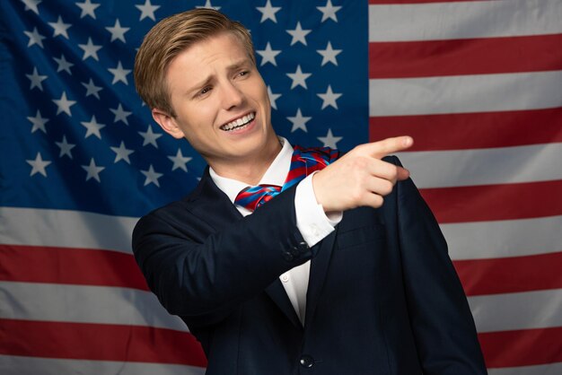 Foto uomo sorridente che punta con il dito lontano sullo sfondo della bandiera americana