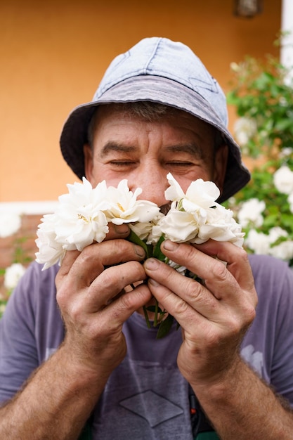 Foto ritratto sorridente dell'uomo che gode dell'aroma delle rose bianche