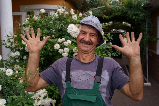 Smiling man portrait with a white rose on his hat with bushes of roses in background