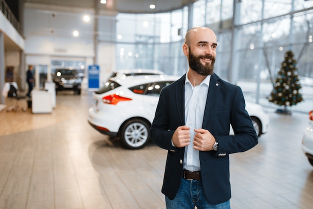 Smiling man poses in car dealership.