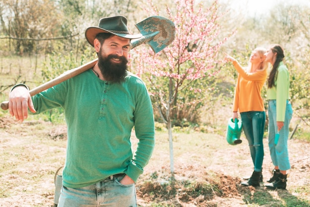 Smiling man preparing to planting Man plants a tree Friends working in garden Group of youth work in spring yard with garden tools