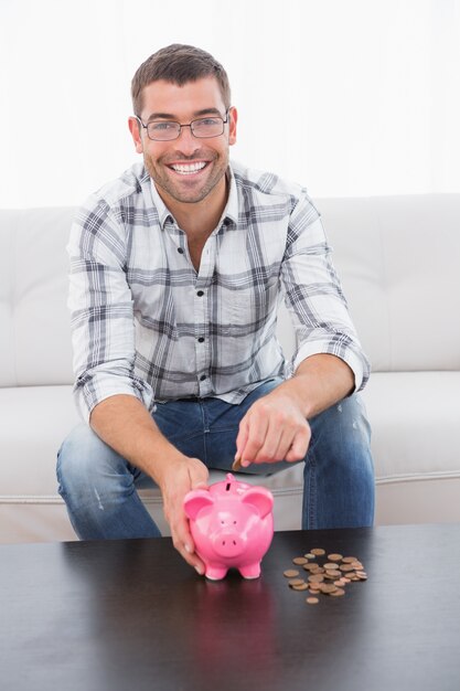 A smiling man putting coins in a piggy bank