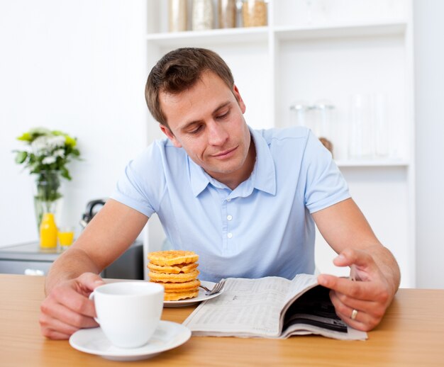 Photo smiling man reading a newspaper while having breakfast