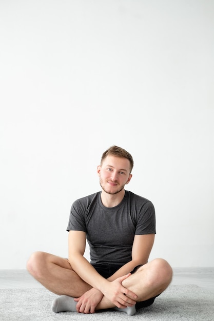 Smiling man Resting home Lockdown training Selfisolation lifestyle Handsome satisfied guy in sportswear sitting floor in lotus pose light wall interior background