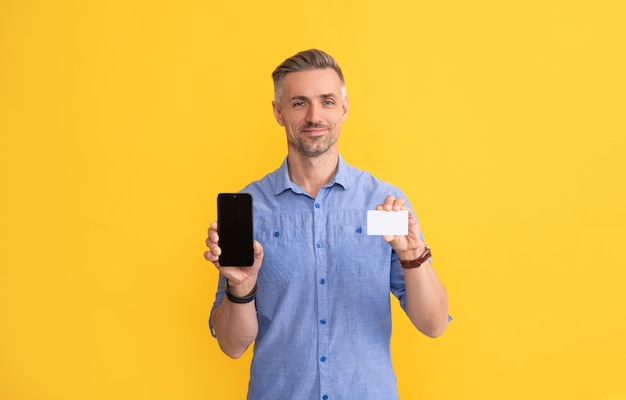 Smiling man showing phone and credit card with copy space internet buy