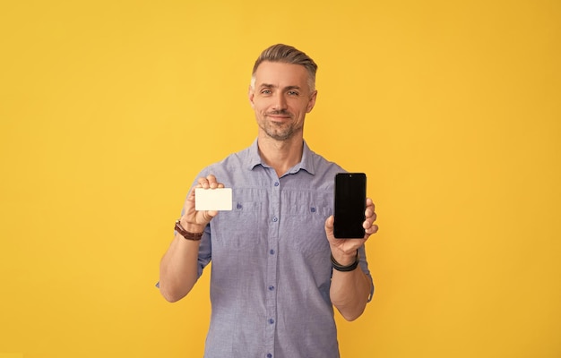 Smiling man showing phone and credit card with copy space internet buy