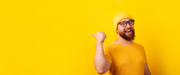 Uomo sorridente che mostra il pollice in su gesto e indica uno spazio vuoto su sfondo giallo, layout panoramico