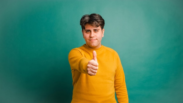 Smiling man showing thumb up in green studio