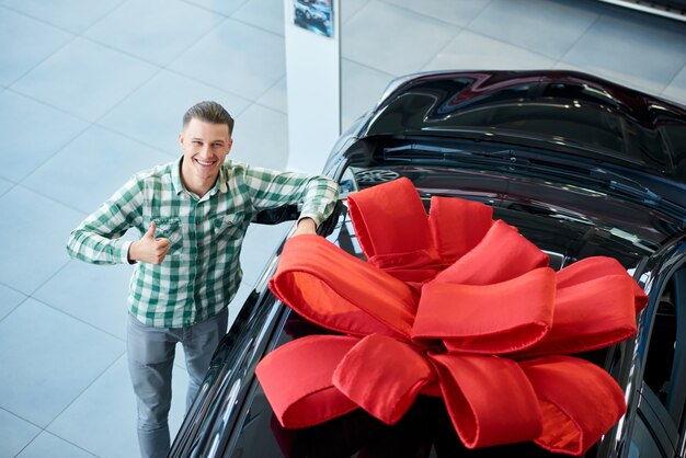 Uomo sorridente che mostra pollice in su vicino all'automobile.