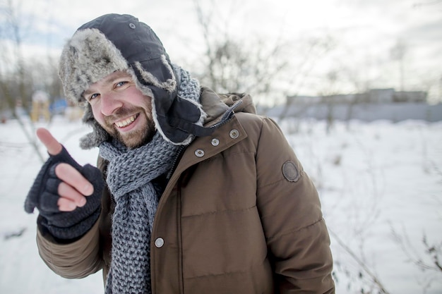 笑顔の男が毛皮の帽子とジャケットで冬の屋外で人差し指を示して説明します