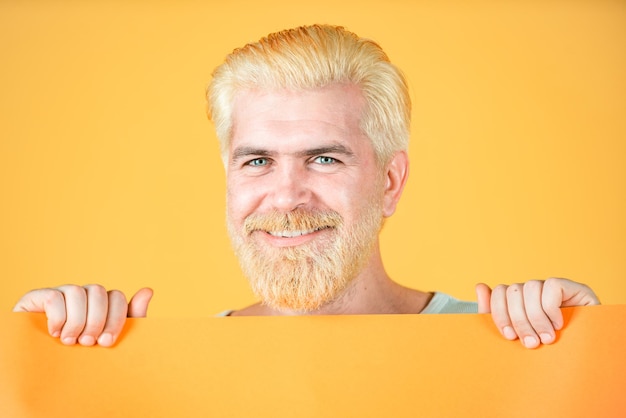 Smiling man shows a sheet of paper in the camera on a yellow background Blank empty paper billboard with copy space for text