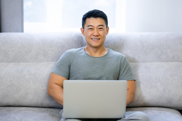 Smiling man sits on a comfortable sofa in the living room relaxes while working on a laptop