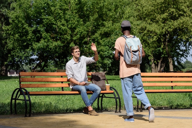 Smiling man sitting on bench and waving to friend in park