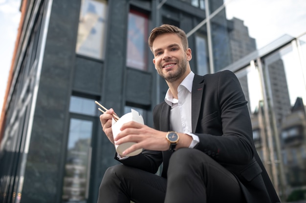 Smiling man sitting on the steps and eating asian food