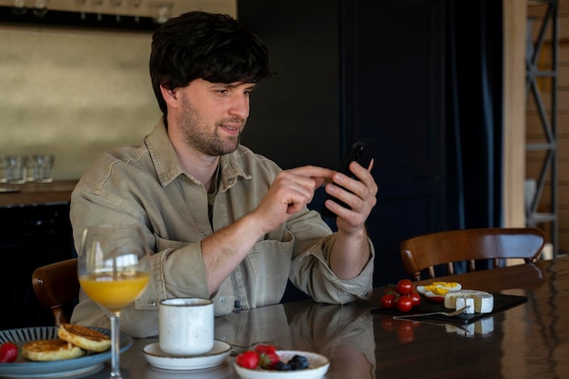 Smiling man sitting at a table in the kitchen with a cup of coffee and looking at a smartphone a man