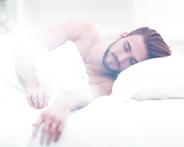Улыбающийся мужчина спит на удобной кровати.