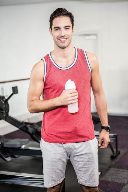 Uomo sorridente che sta e che tiene bottiglia di acqua in palestra