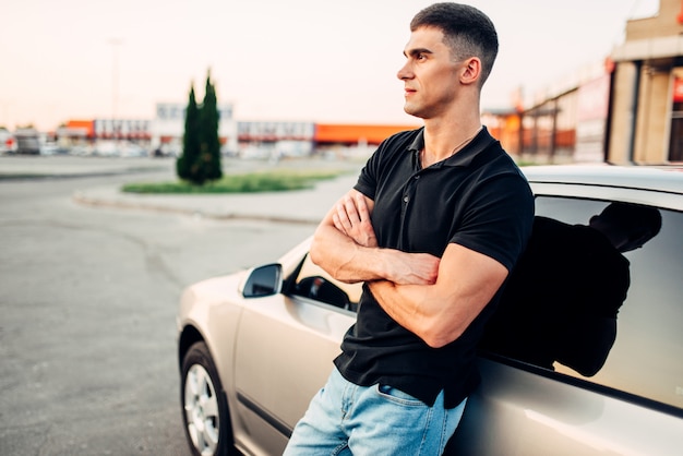 彼の車の近くに屋外に立っている笑顔の男