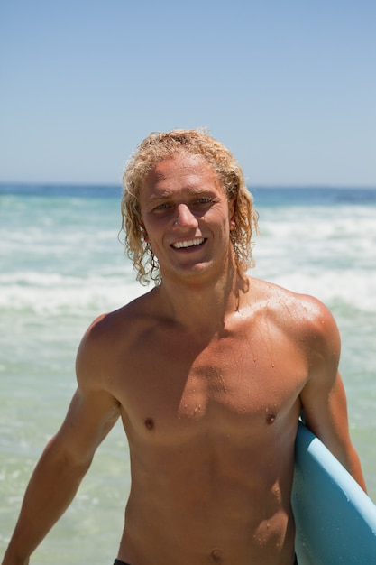 Photo smiling man standing in the water while holding his surfboard