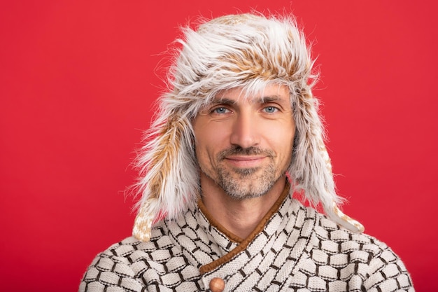 Smiling man in sweater and earflap on red background winter