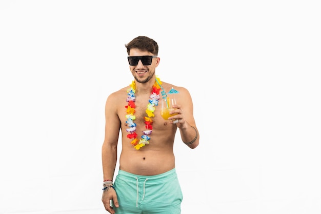 Smiling man in swim trunks with flower necklace and sunglasses holding cocktail on white background