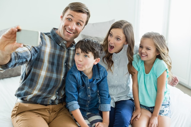 Smiling man taking selfie with family while sitting in bedroom