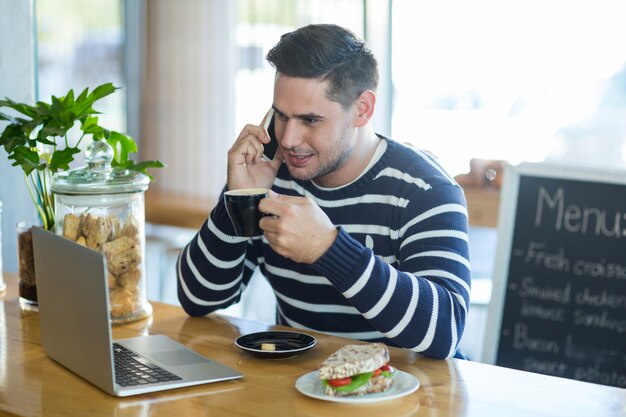 コーヒーを飲みながら携帯電話で話している笑みを浮かべて男