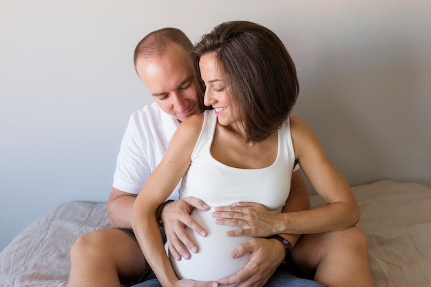 Foto uomo sorridente che tocca la pancia di una donna incinta sul letto a casa