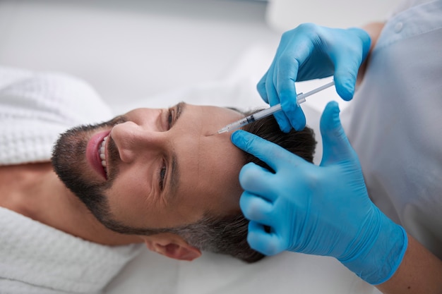 Smiling man undergoes skin lifting procedure lying on couch  