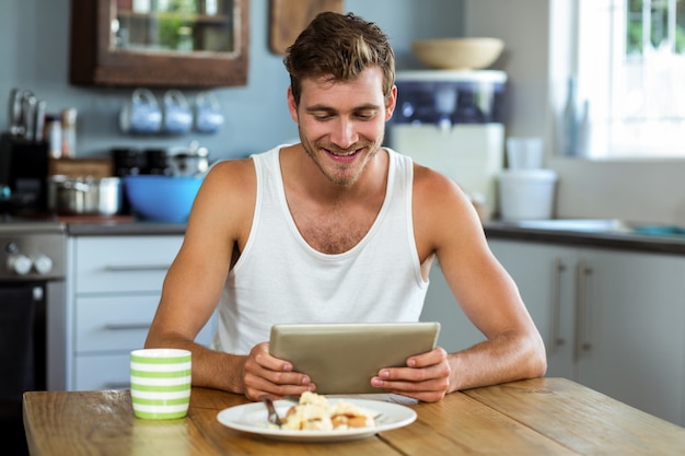 朝食のテーブルでデジタルタブレットを使用して笑みを浮かべて男