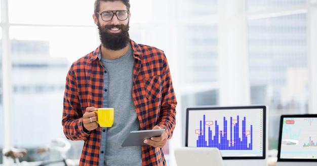 Smiling man using digital tablet while having cup of coffee in office