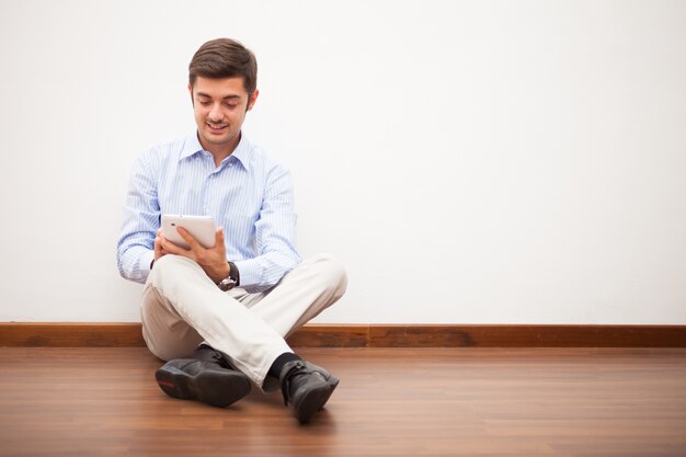 Smiling man using a digital tablet while sitting on the floor of his apartment