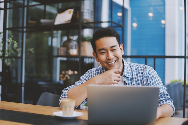 Photo smiling man using laptop while sitting in cafe